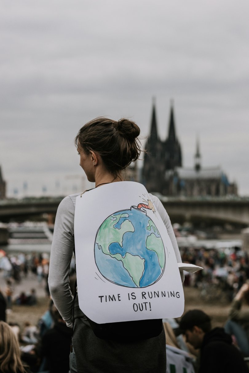 Back view of a woman demonstrator carrying a sign reading "Time is running out!" with an illustration of the planet.