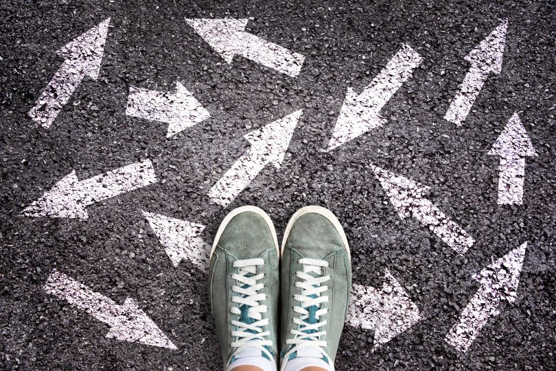 Chaussures de sport et nombreuses flèches pointant dans des directions différentes sur un sol asphalté, concept de choix de vie et d'études difficiles pour l'avenir.